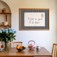 Framed poster with 'it feels so good to be home' quote above a wooden table with decor items.