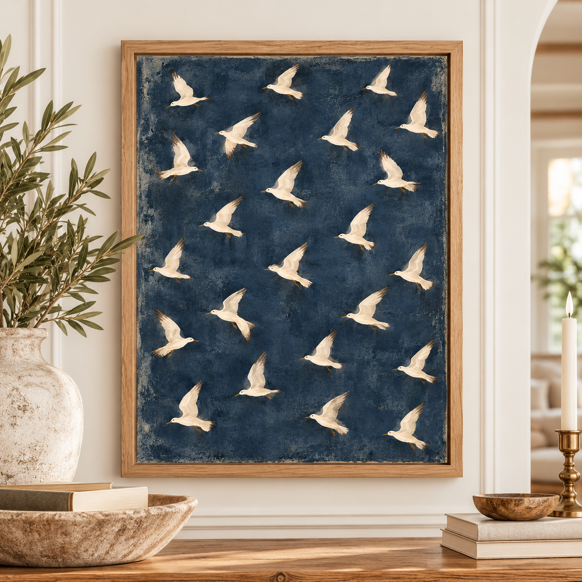 Coastal bird artwork in a natural wood frame displayed on a wooden entryway table with blue hydrangeas, white coral, and neutral beach house accessories.