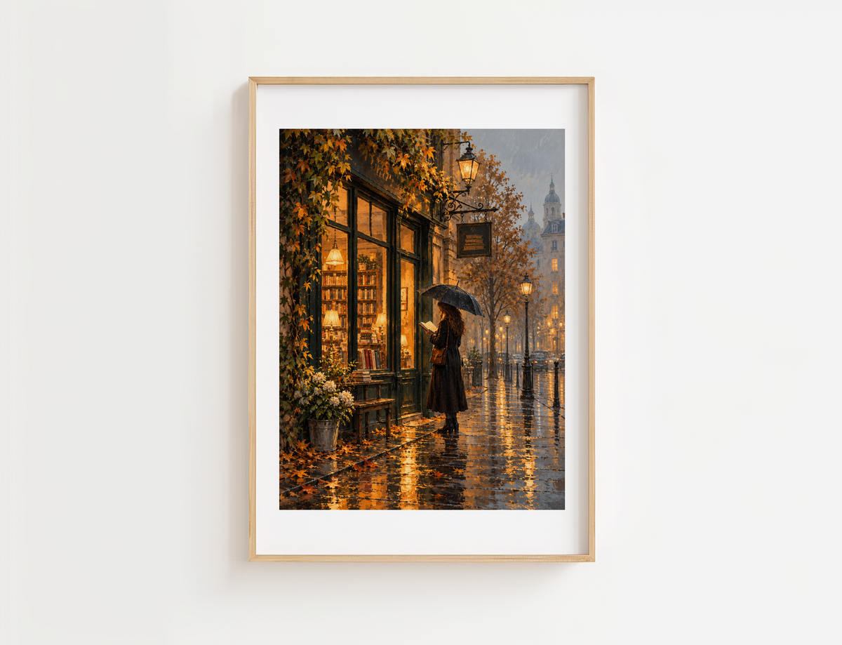 Vintage bookstore wall art featuring a cozy rainy autumn street scene, displayed in a natural wood frame with white matting above a reading nook chair, surrounded by bookshelves, warm fall decor, and soft natural light.