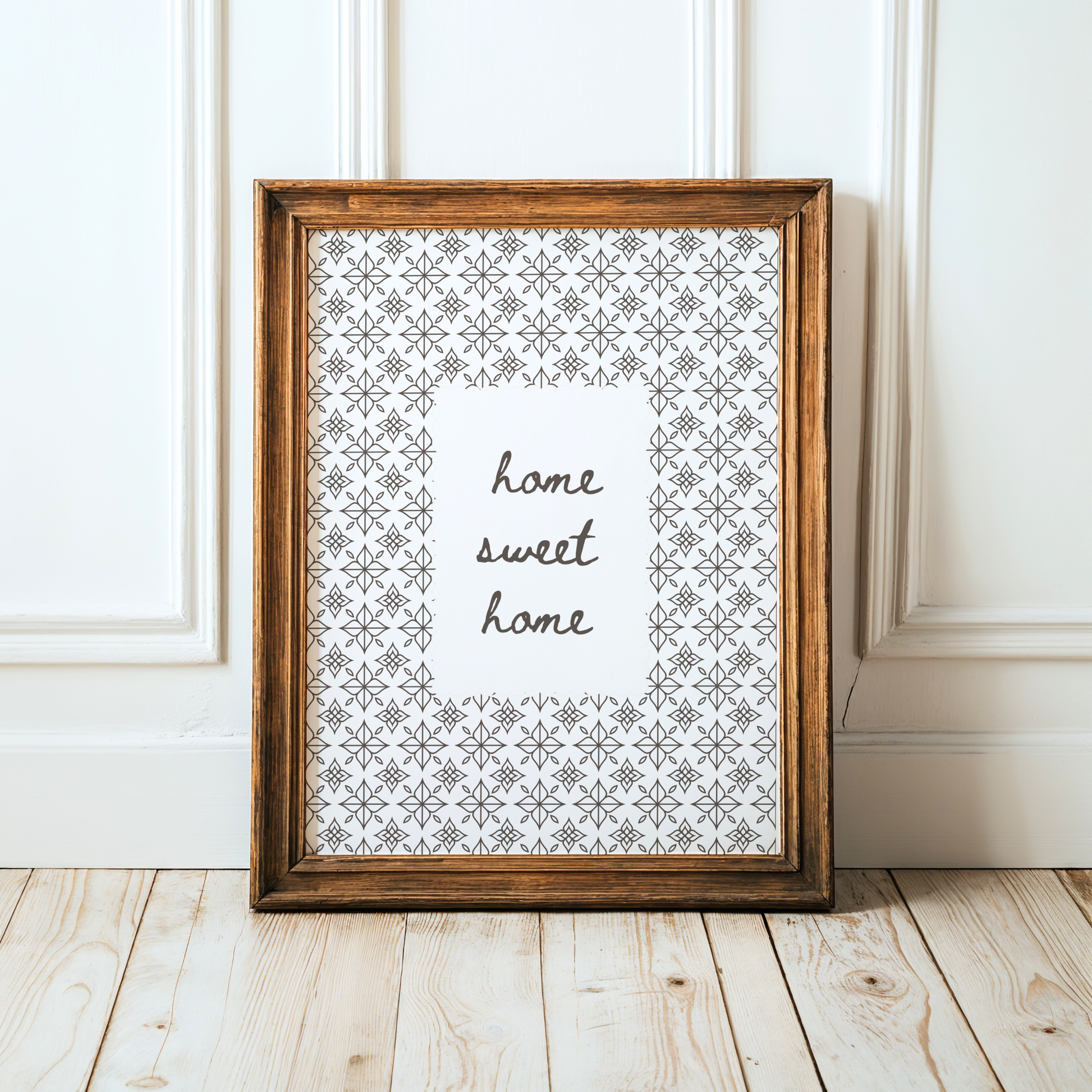 Framed print with 'home sweet home' text on a white background, leaning against a white wall.