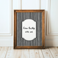 Framed black and white striped poster with 'how lucky are we' text on a wooden floor.