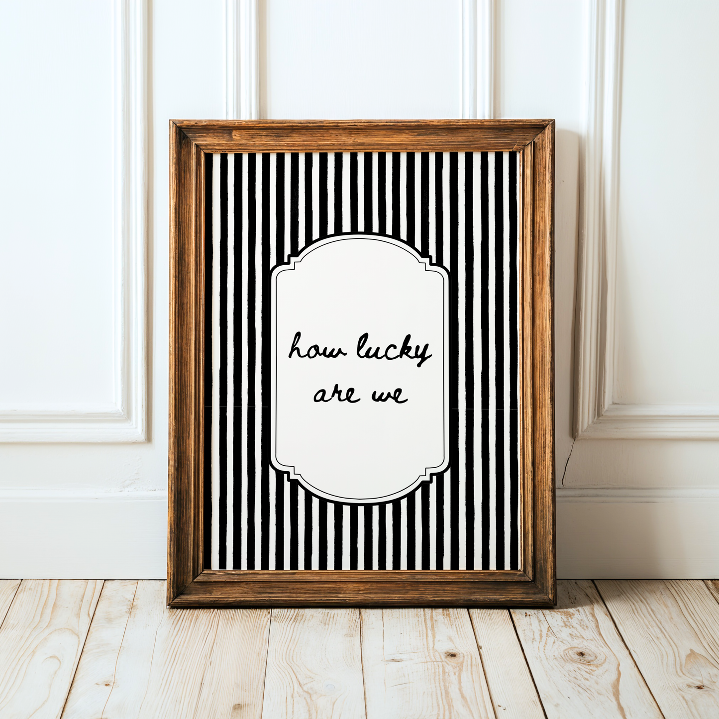 Framed black and white striped poster with 'how lucky are we' text on a wooden floor.