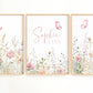 Three framed watercolor floral prints with butterflies hang on a white wall. The center print has the names 'Sophia' and 'LYNN' in pink script, while the side prints show pastel flowers and green stems.