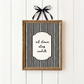 Framed black and white striped print with 'sit down stay awhile' text on a white wooden background.