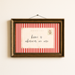 Framed postcard with red and white striped border and 'home is wherever we are' text on a beige wall.