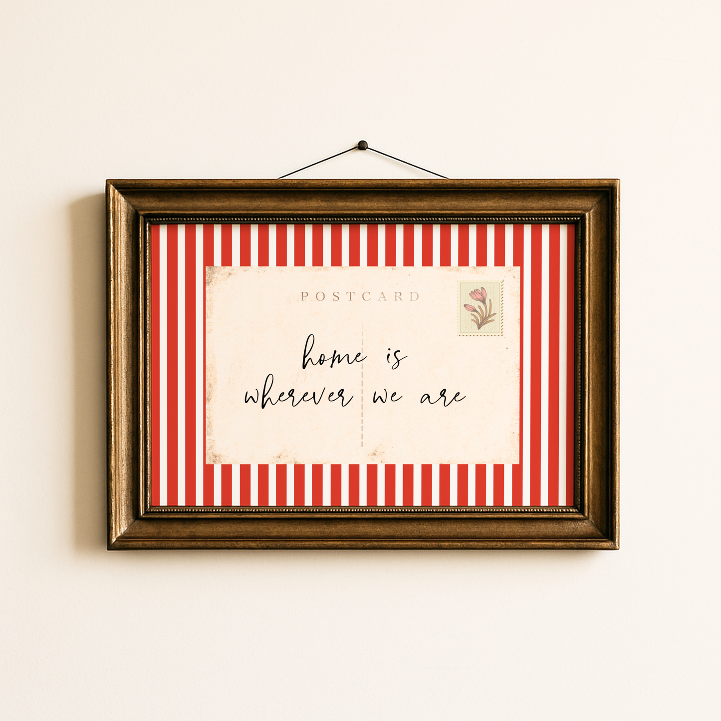 Framed postcard with red and white striped border and 'home is wherever we are' text on a beige wall.