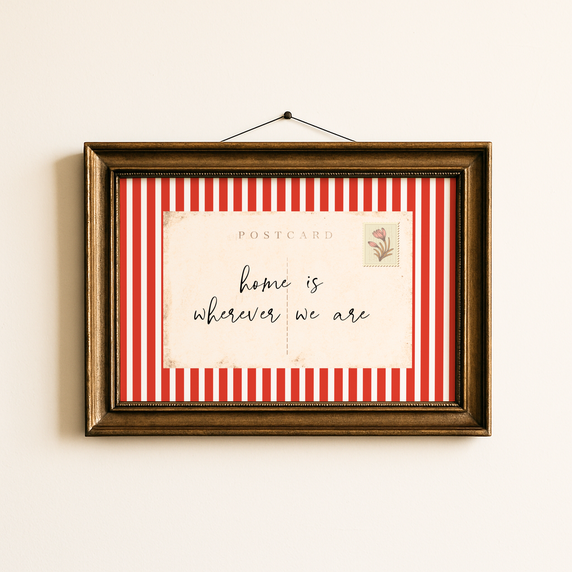 Framed postcard with red and white striped border and 'home is wherever we are' text on a beige wall.